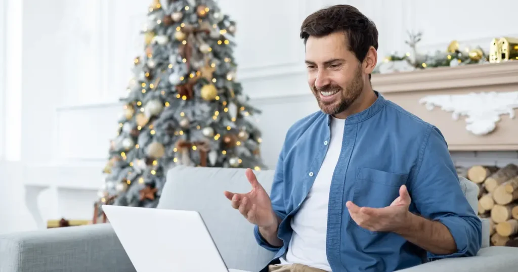 Man with laptop sitting in front of Christmas tree