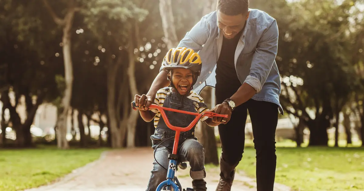 Father teaches young child to ride a bike in sunny park.