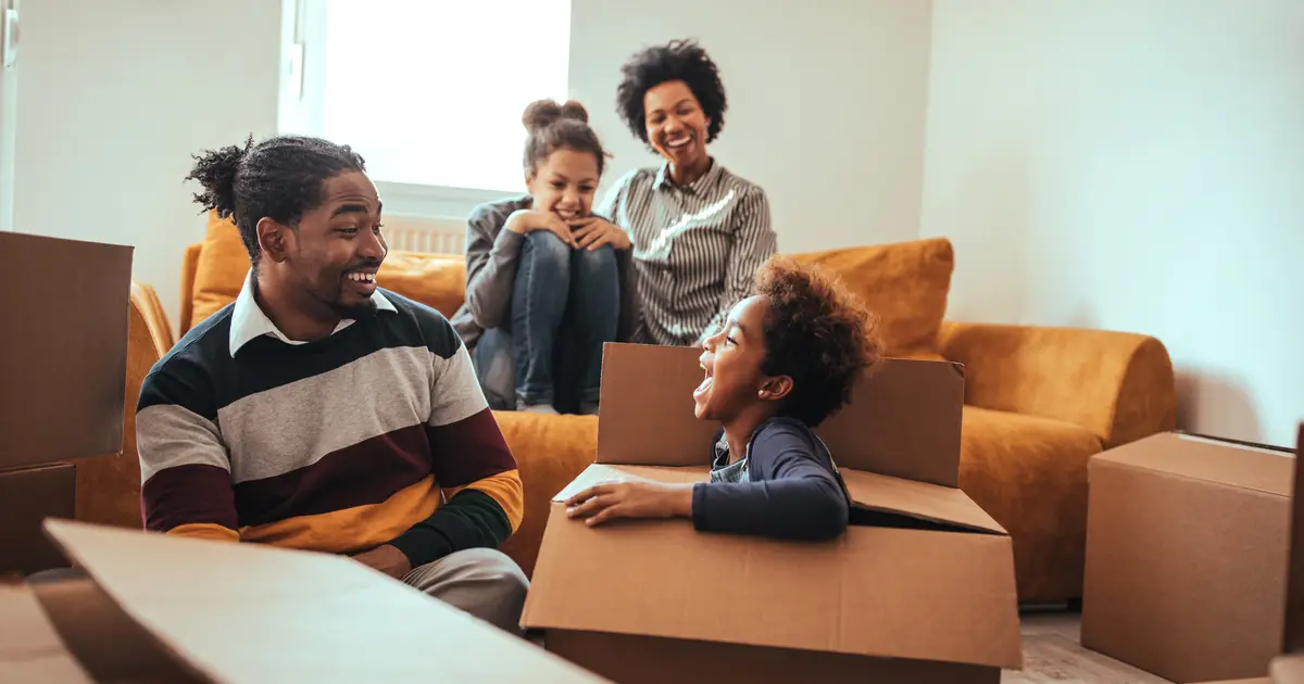 Family unpacks in new home as daughter laughs inside moving box.