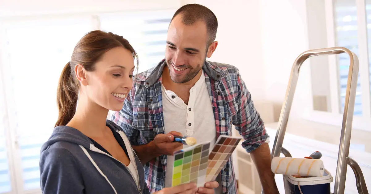 Smiling couple discusses paint swatches in a room they’re renovating.