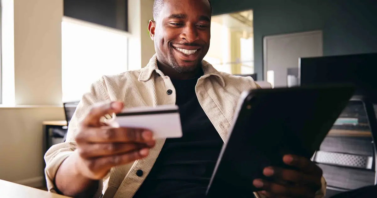 Smiling man holding credit card and tablet