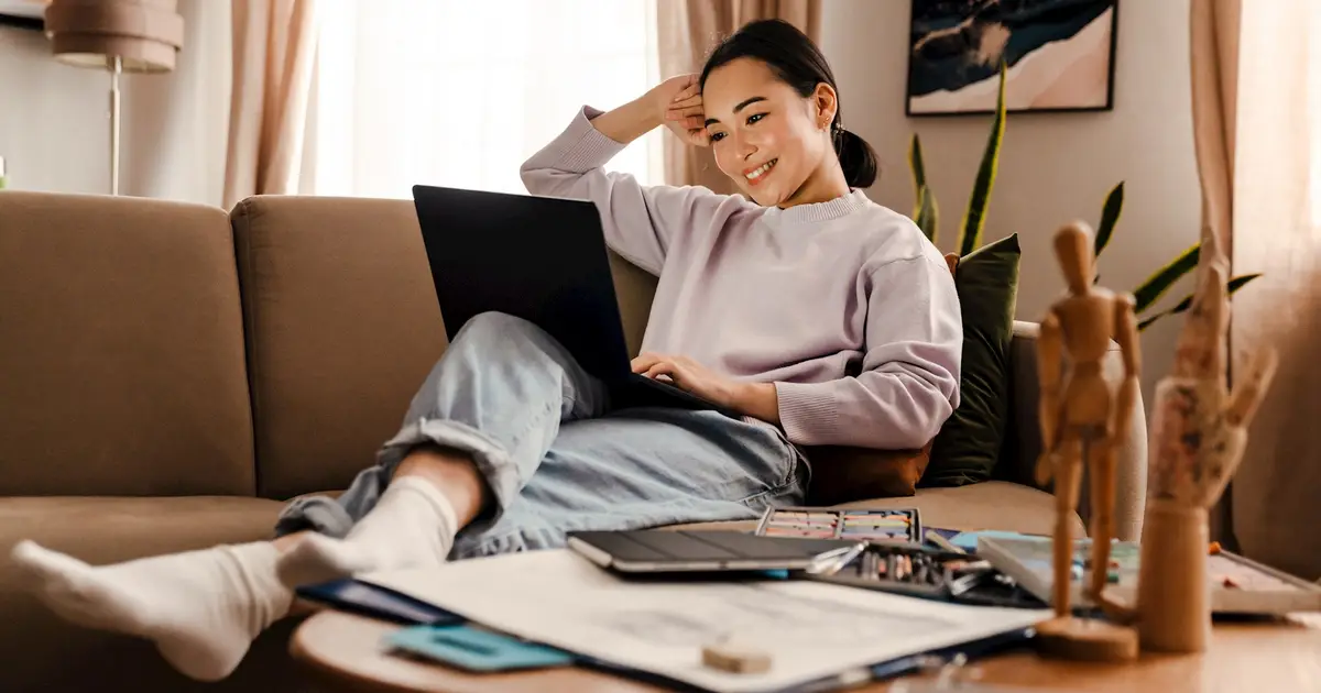 Young woman smiling on couch, using laptop in cozy living room.