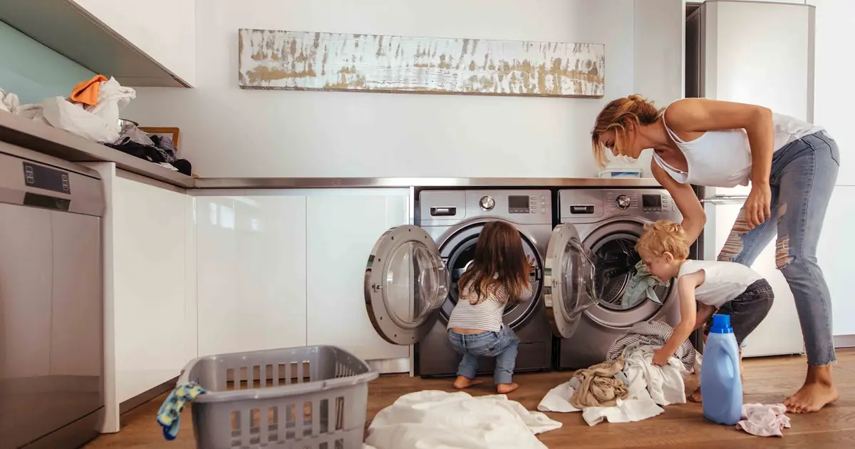 Woman and children loading laundry into washing machine.