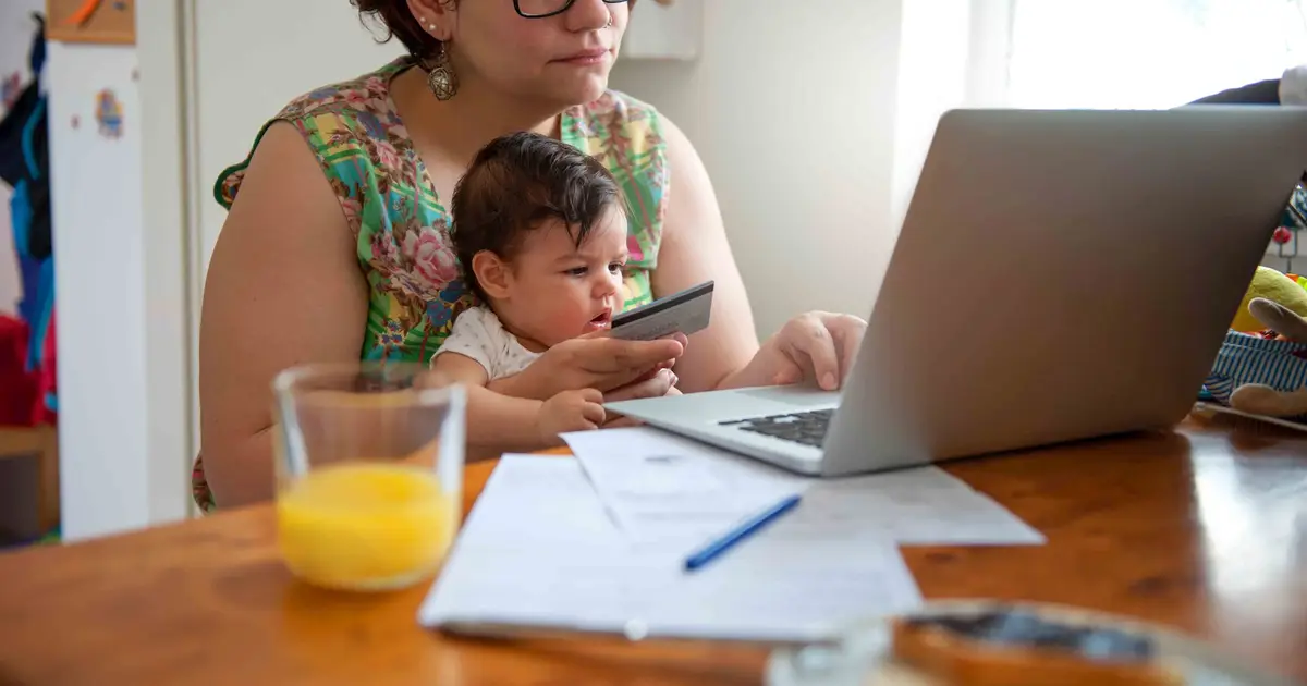 Woman holding baby and using laptop.