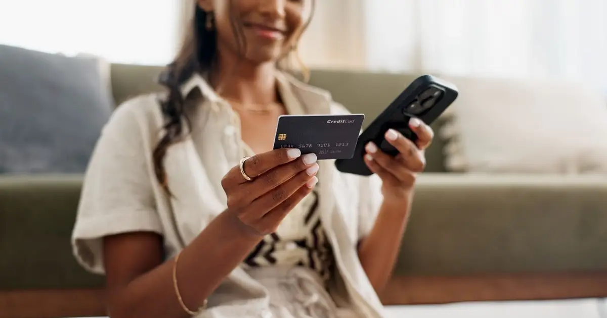 Woman holding a credit card and smartphone, preparing for an online transaction.