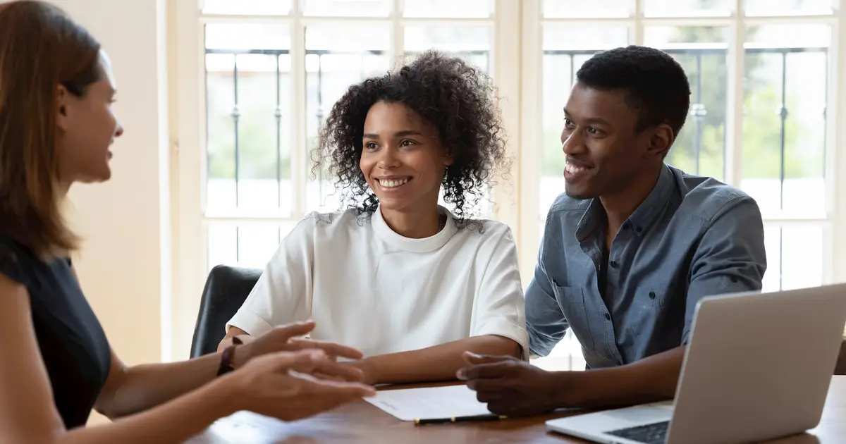 Smiling couple discussing mortgage options with advisor, documents on table.