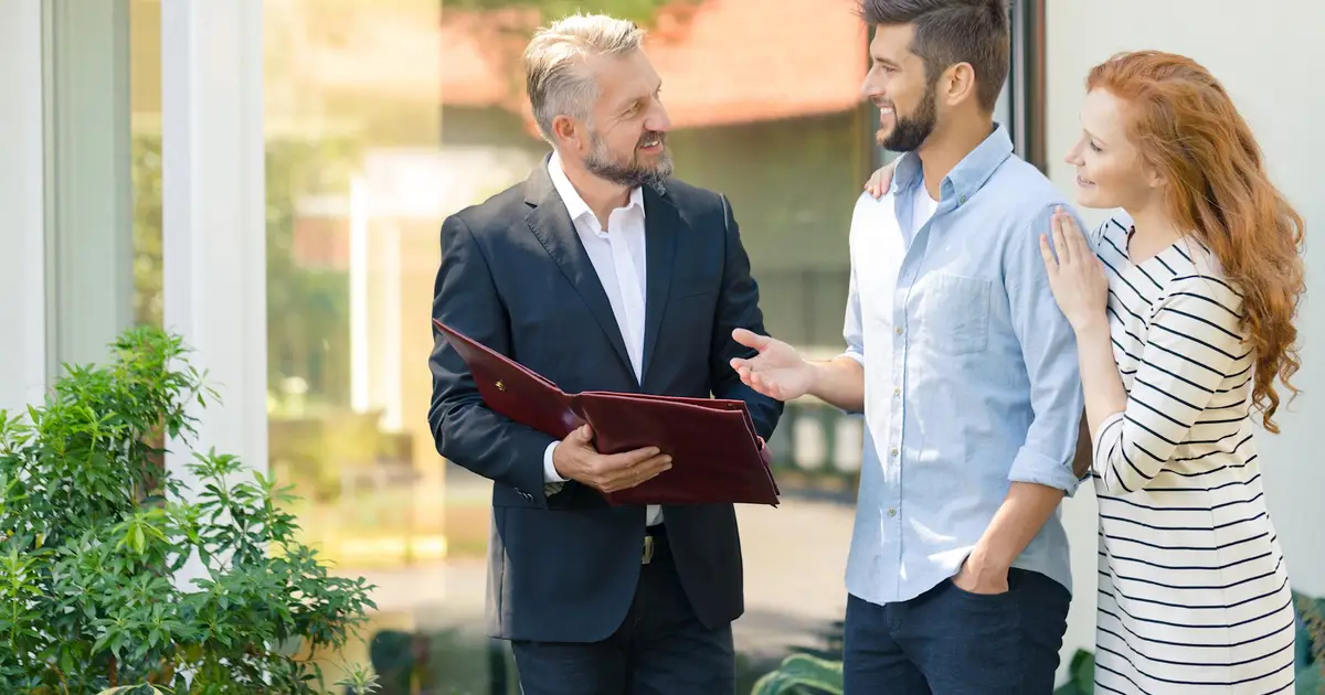 Real estate agent speaking with a smiling couple outdoors.