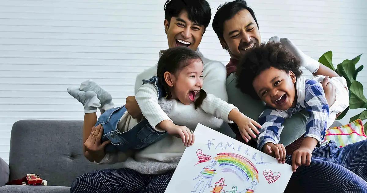 Joyful family of four holding a colorful “Family” rainbow drawing.