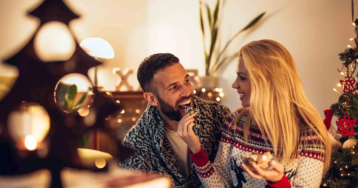 Couple enjoying holidays near tree and festive lights.