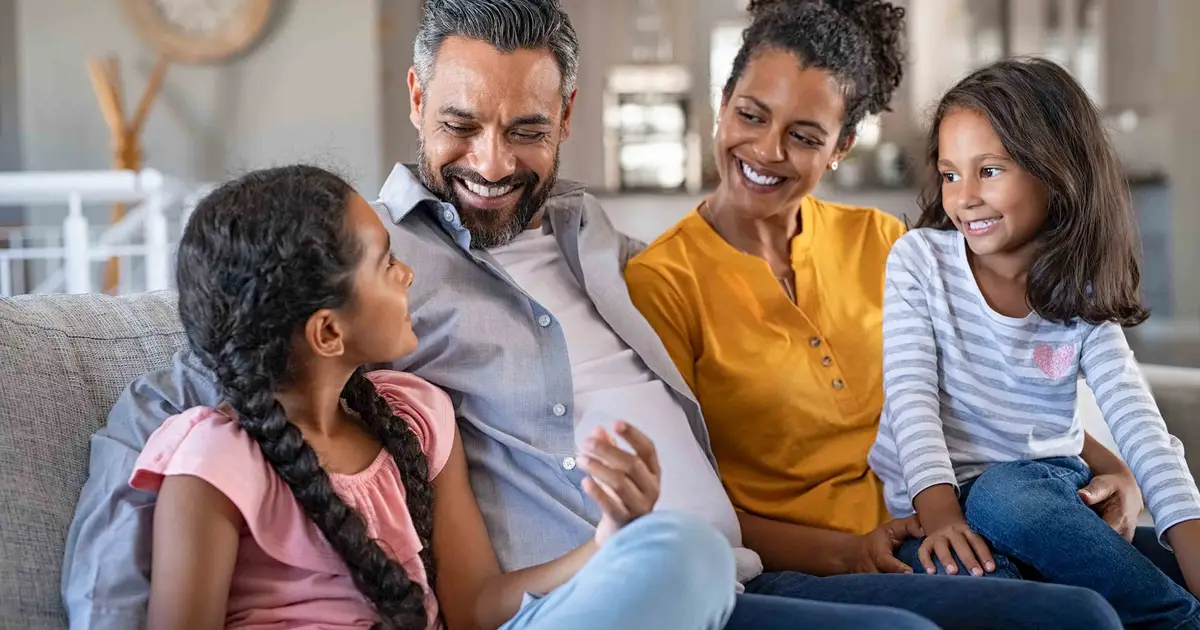 Happy family on couch, parents smiling at two young daughters.