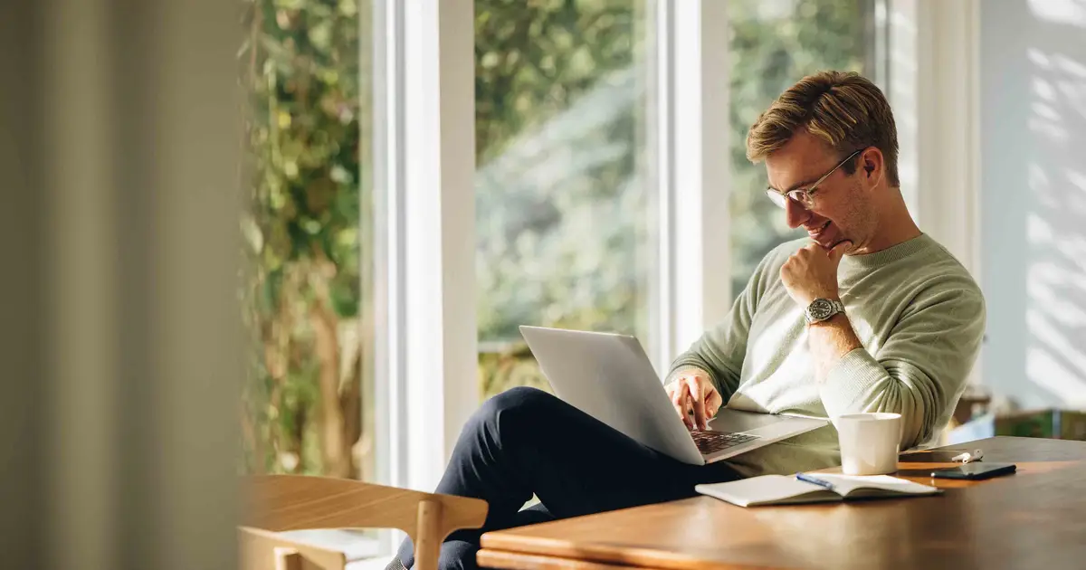 Man working on laptop by a window.