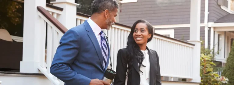Two real estate professionals walking outside of a house while talking.