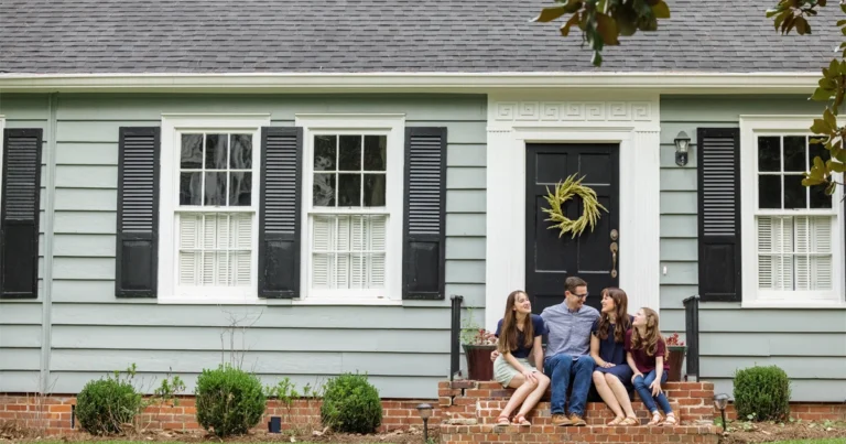 Smiling family sits on steps of their home.