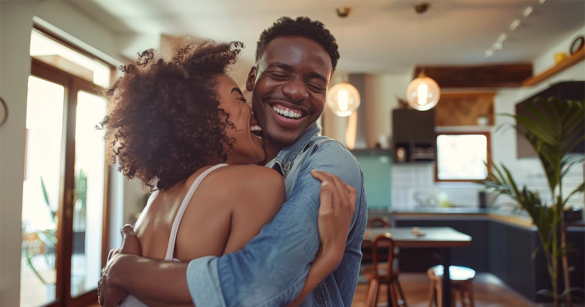 Young couple embraces and laughs in kitchen.
