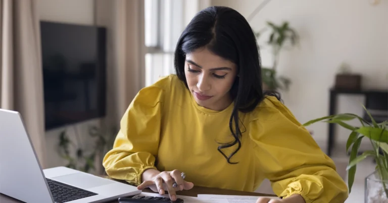 Woman calculating finances with laptop and documents.