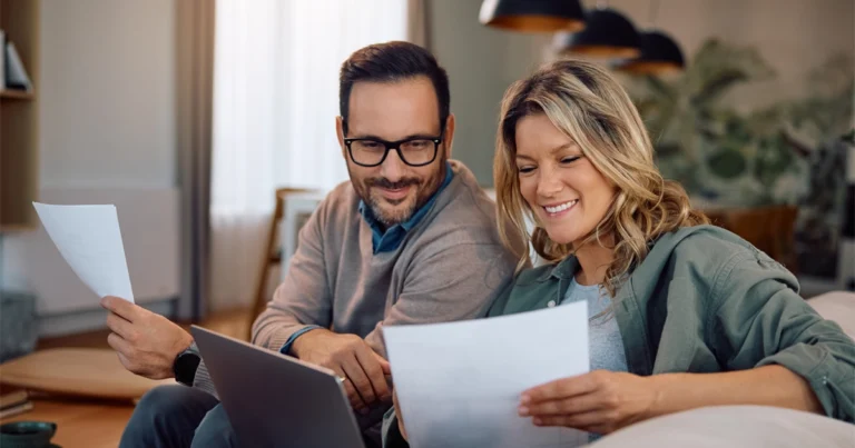 Smiling couple reviews documents on couch.