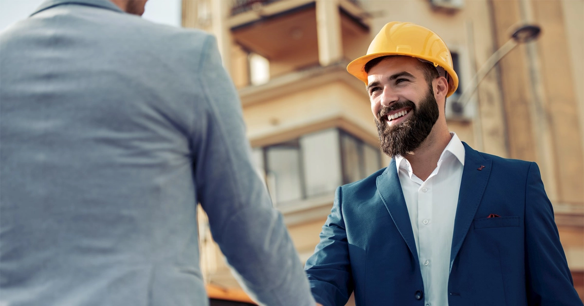 A business man in a construction hat shaking hands.
