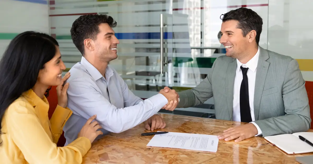 Smiling couple shaking hands with agent